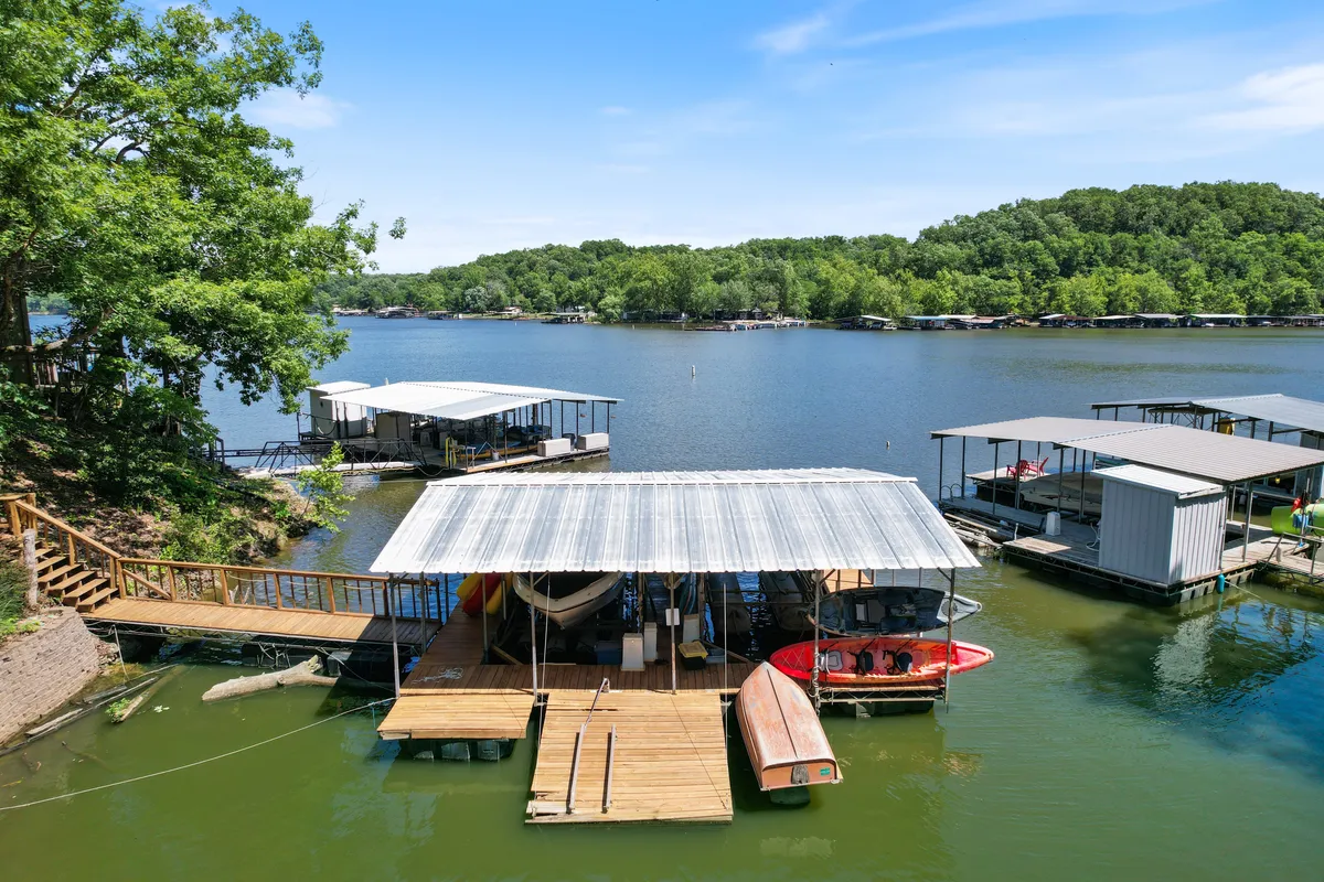 A wide-angle shot of the lakeshore features boathouses, a wooden dock, and boats bobbing on calm water under an expansive sky. The scene exudes a peaceful atmosphere ideal for reflection, fishing, and lakeside relaxation.