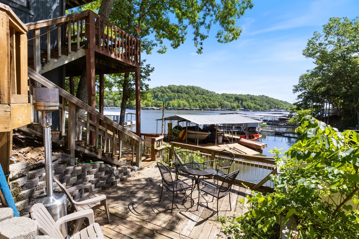 An inviting outdoor seating area overlooking the lake, with steps leading to an upper deck. The space is surrounded by greenery, offering sweeping views of the water, perfect for entertaining guests, relaxing, or watching the sunset.