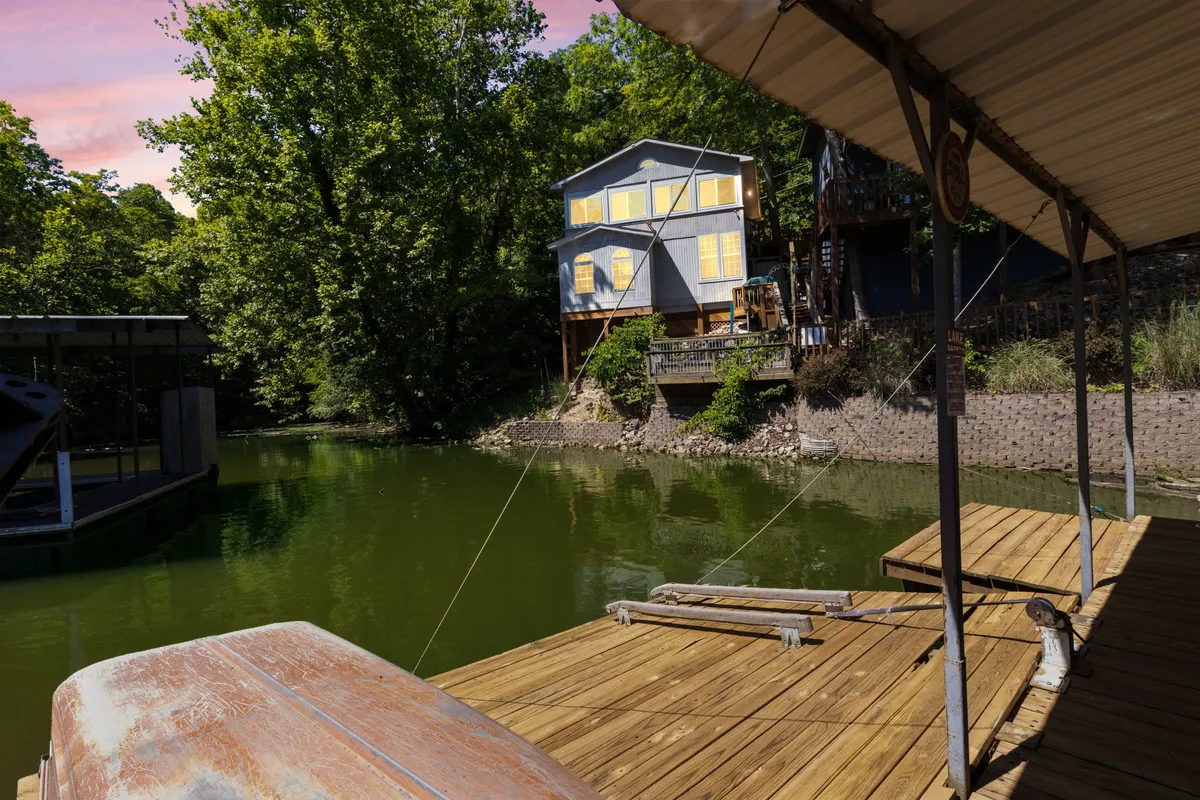 A tranquil scene featuring a wooden dock extending into calm water, with the waterfront house nestled among lush greenery. The dock is perfectly suited for fishing, launching a kayak, or simply relaxing while taking in panoramic views of Indian Creek Cove.