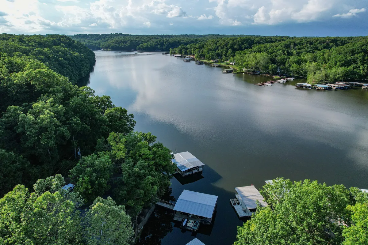 A sweeping view of a calm river lined with dense greenery and several boathouses. The sunset casts a warm glow over the water, inviting visitors to enjoy activities like fishing, boating, or wildlife watching amid scenic natural surroundings.