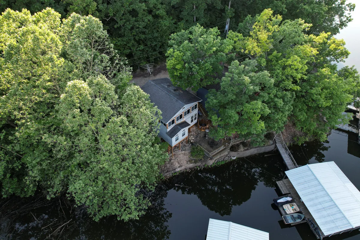This exterior image captures the retreat house enveloped by tall trees, the private dock extending into the water, and the tranquil lake just beyond. The overall scene radiates peaceful seclusion and natural beauty, emphasizing the setting's remoteness and the connection between home and water.