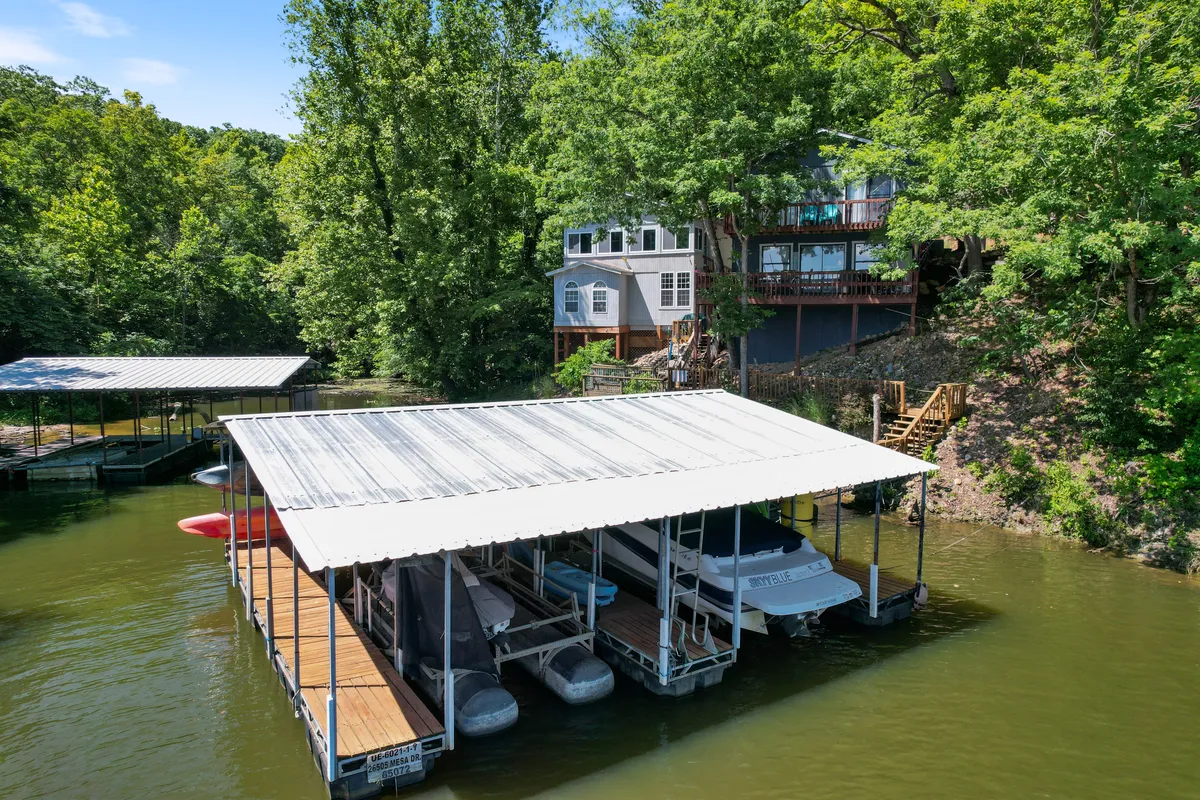 A tranquil lakeside scene featuring a boathouse, watercraft, and a home perched on a hill surrounded by trees. The dock and boats highlight opportunities for fishing, paddling, and enjoying life on the water, with a serene atmosphere perfect for family relaxation.