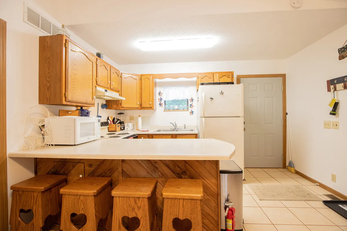 This image highlights a spacious kitchen featuring a central island with stools, warm wooden cabinetry, and a window with curtains. The space radiates a homey and welcoming atmosphere, perfect for meal preparation and casual gatherings. The layout supports both collaborative cooking and relaxed dining.