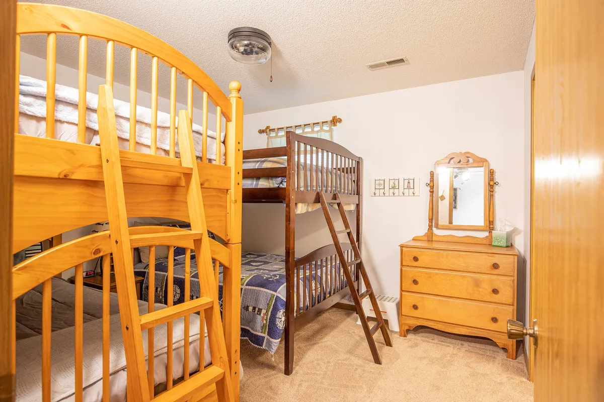 A playful bedroom scene featuring bunk beds, a dresser, and a mirror. The room is styled to welcome children or groups, with the mood suggesting fun activities like playing games or sharing bedtime stories, emphasized by touches like playful bedding and ample space for creativity.